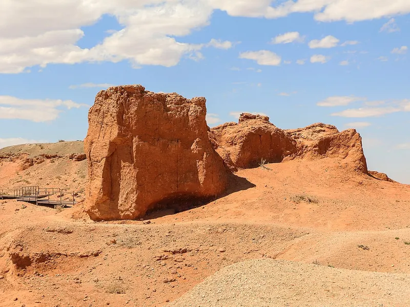 Red sandstone buttes rising from a sandy desert under a blue sky